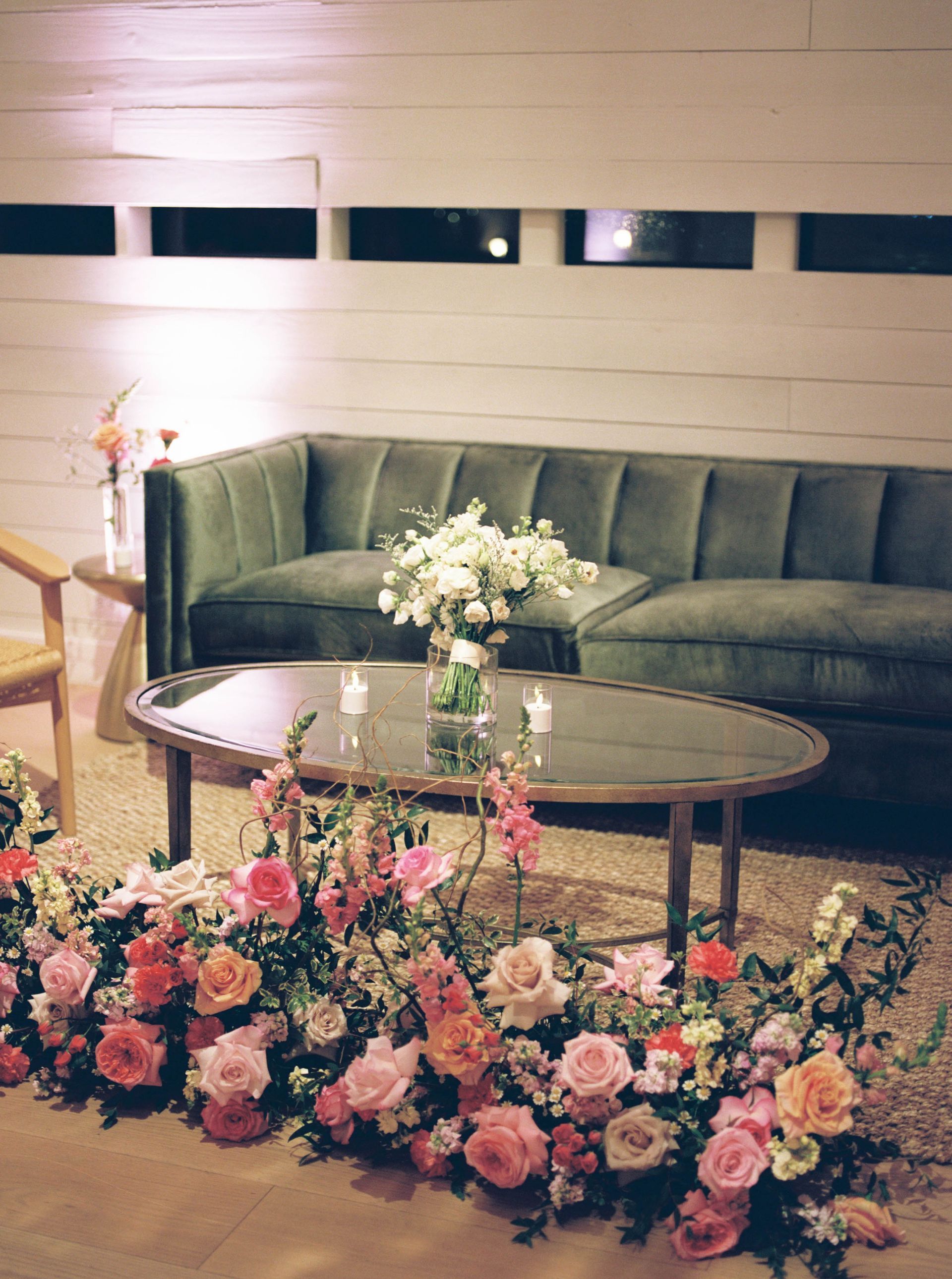 Green velvet sofa, oval table with flowers, and a floor floral arrangement.