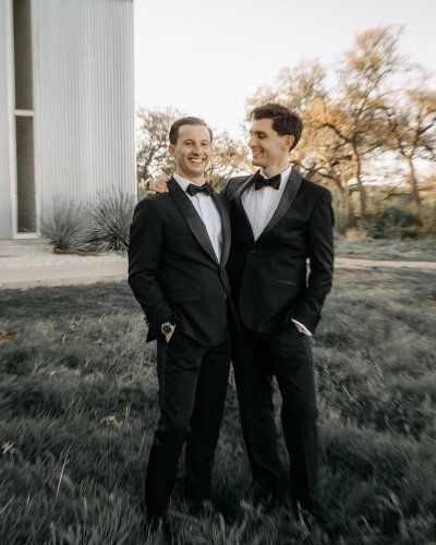 Two men in tuxedos are standing next to each other in a field.
