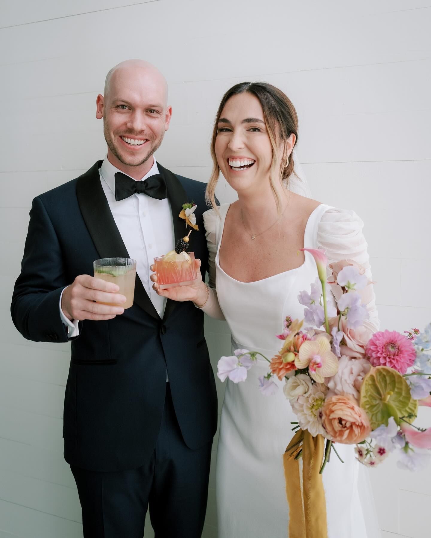 A bride and groom are posing for a picture while holding drinks.