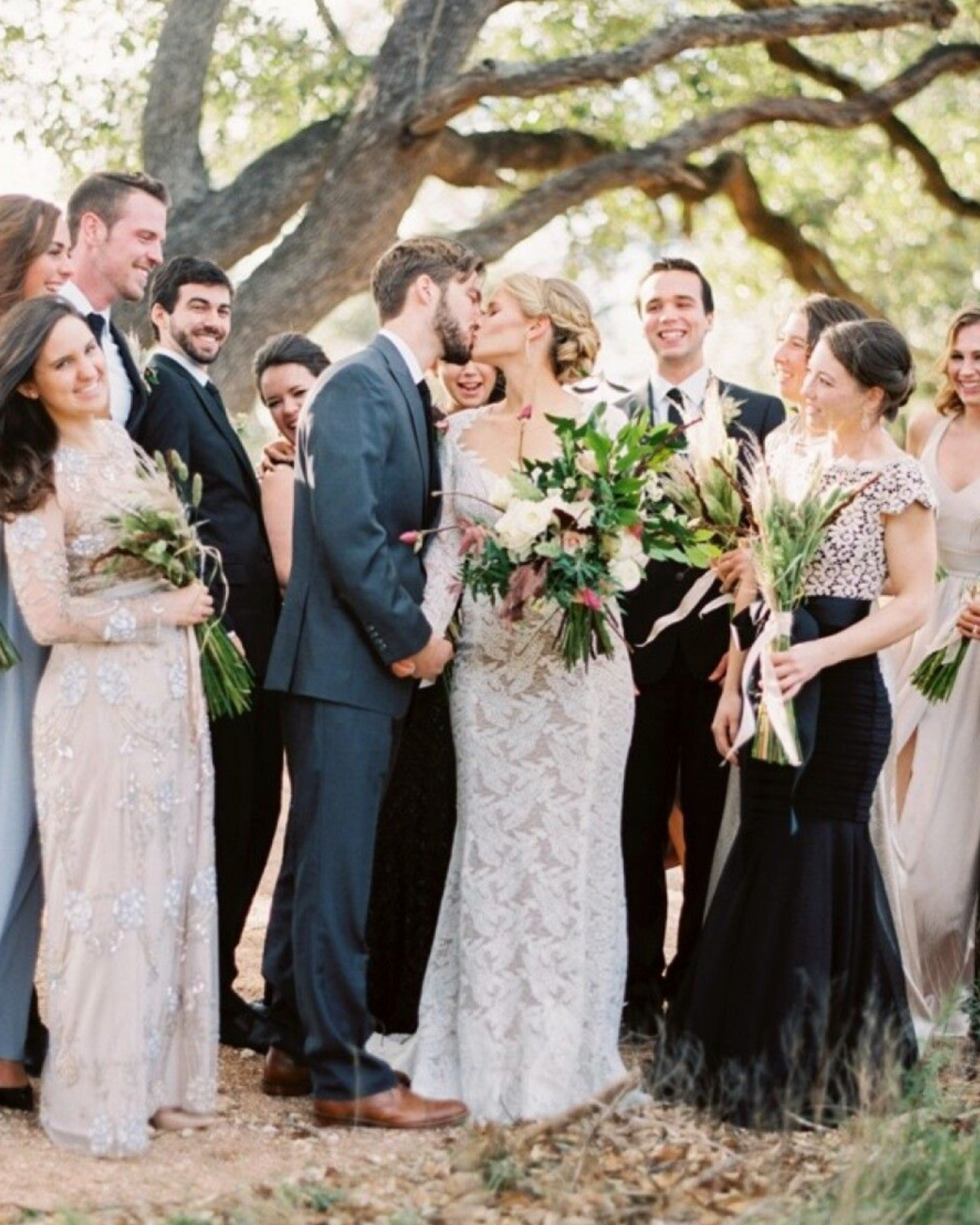 A bride and groom are kissing in front of their wedding party.