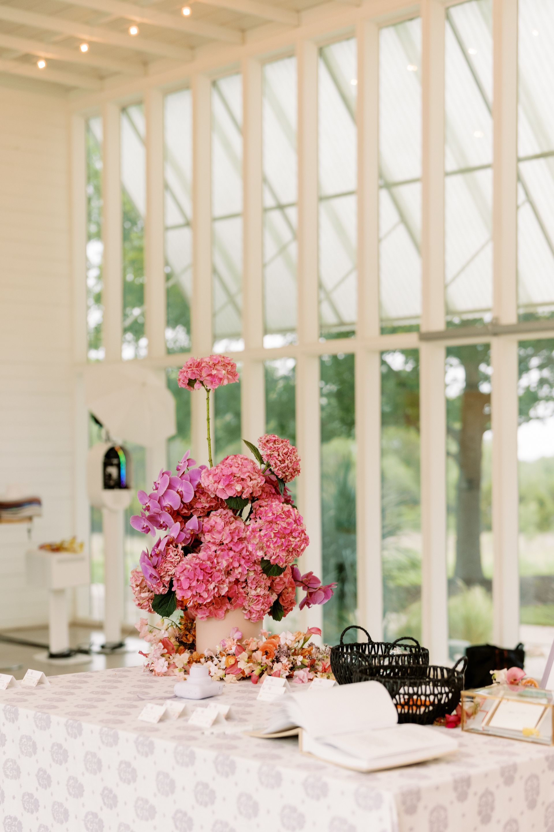 Pink flower arrangement on a table. Large windows in background.
