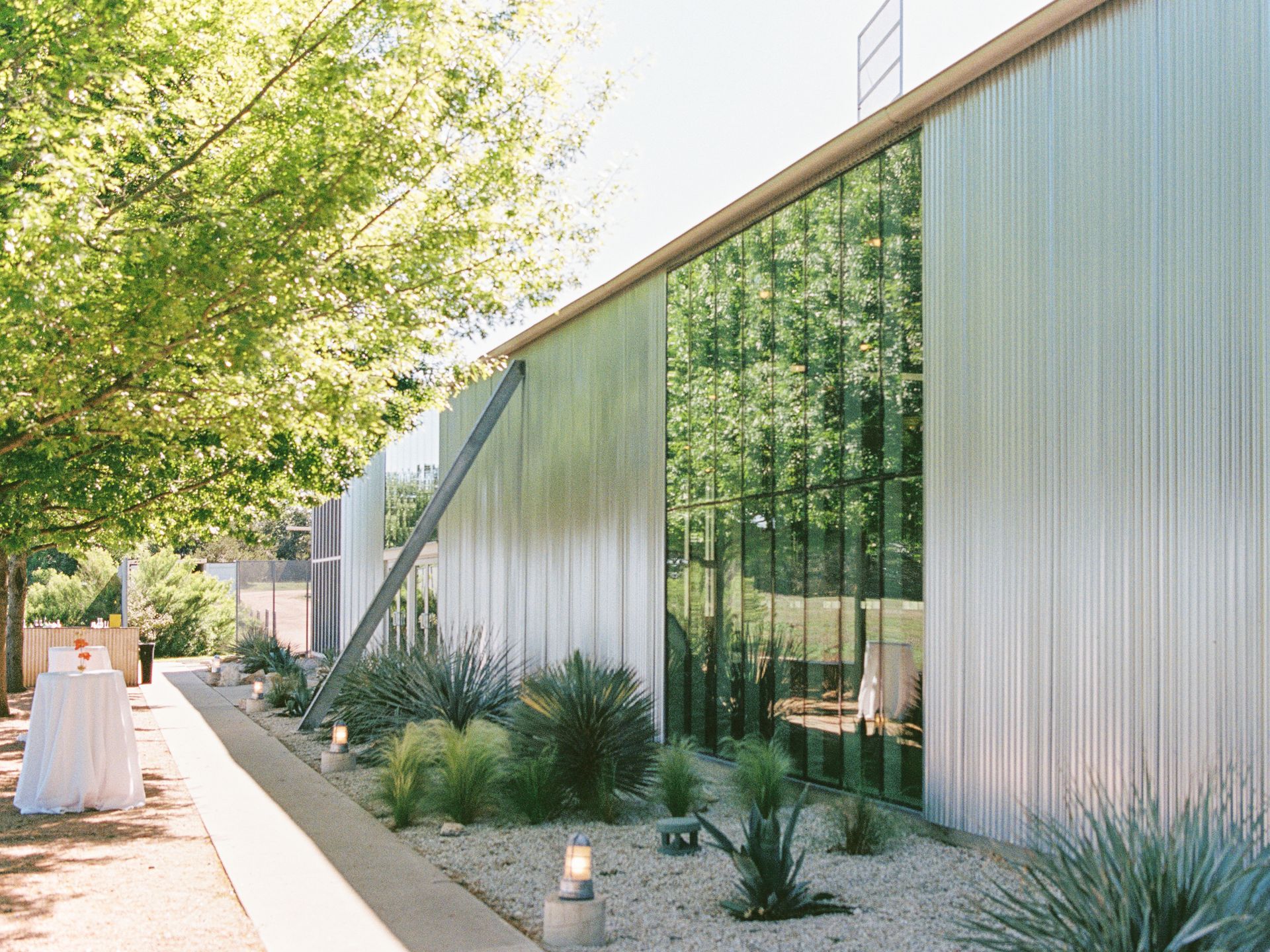 Modern building with corrugated metal siding and large glass windows, next to a pathway with plants.