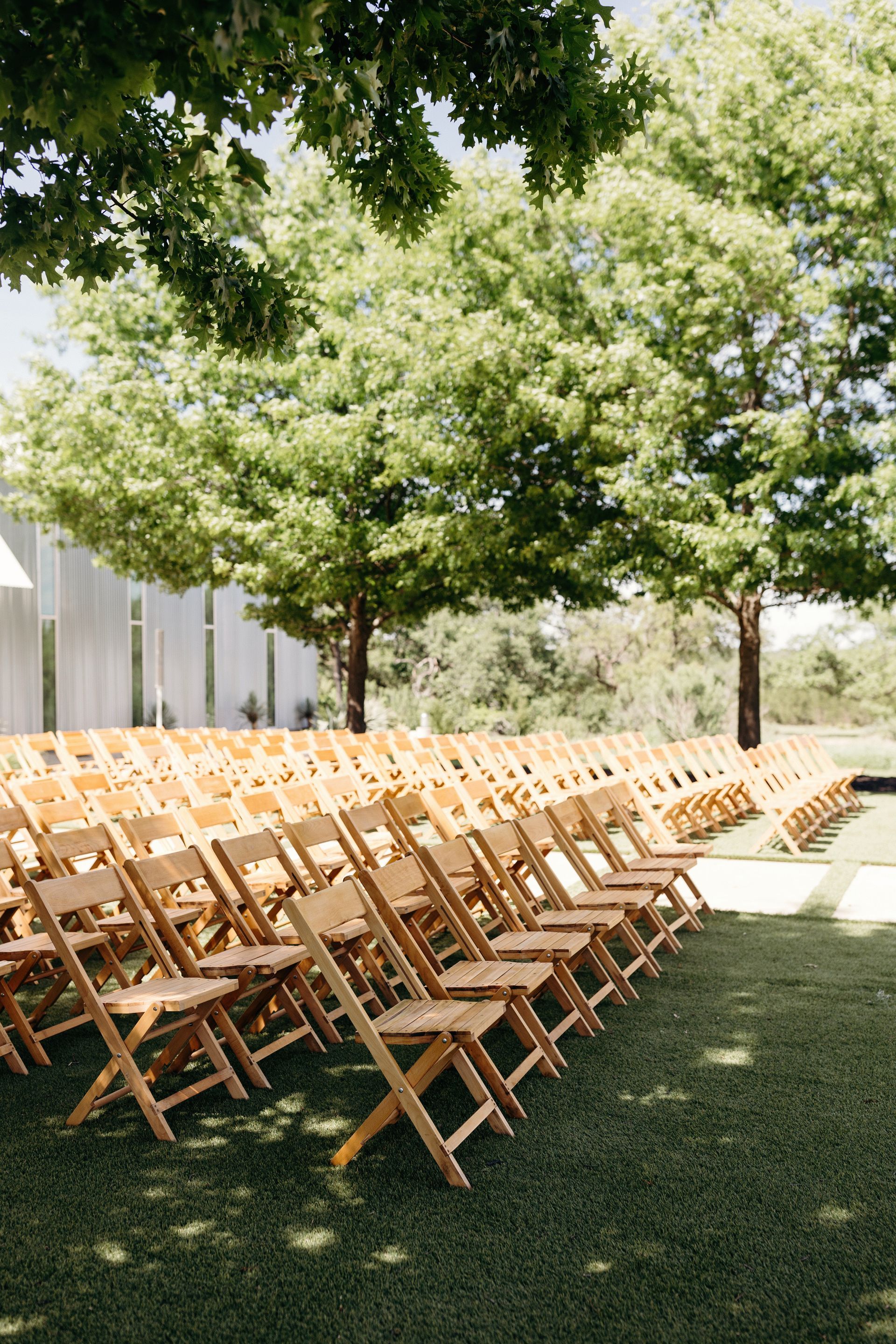 A row of wooden folding chairs sitting on top of a lush green field.