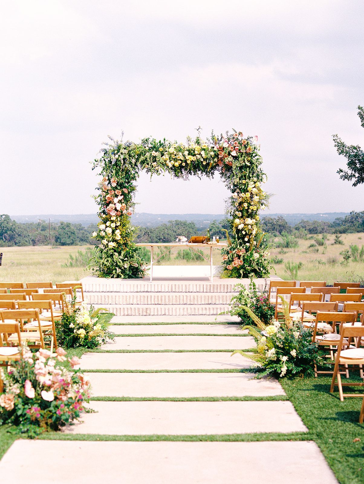 Wedding ceremony setup: Floral archway with rows of chairs, outdoor setting, natural light.
