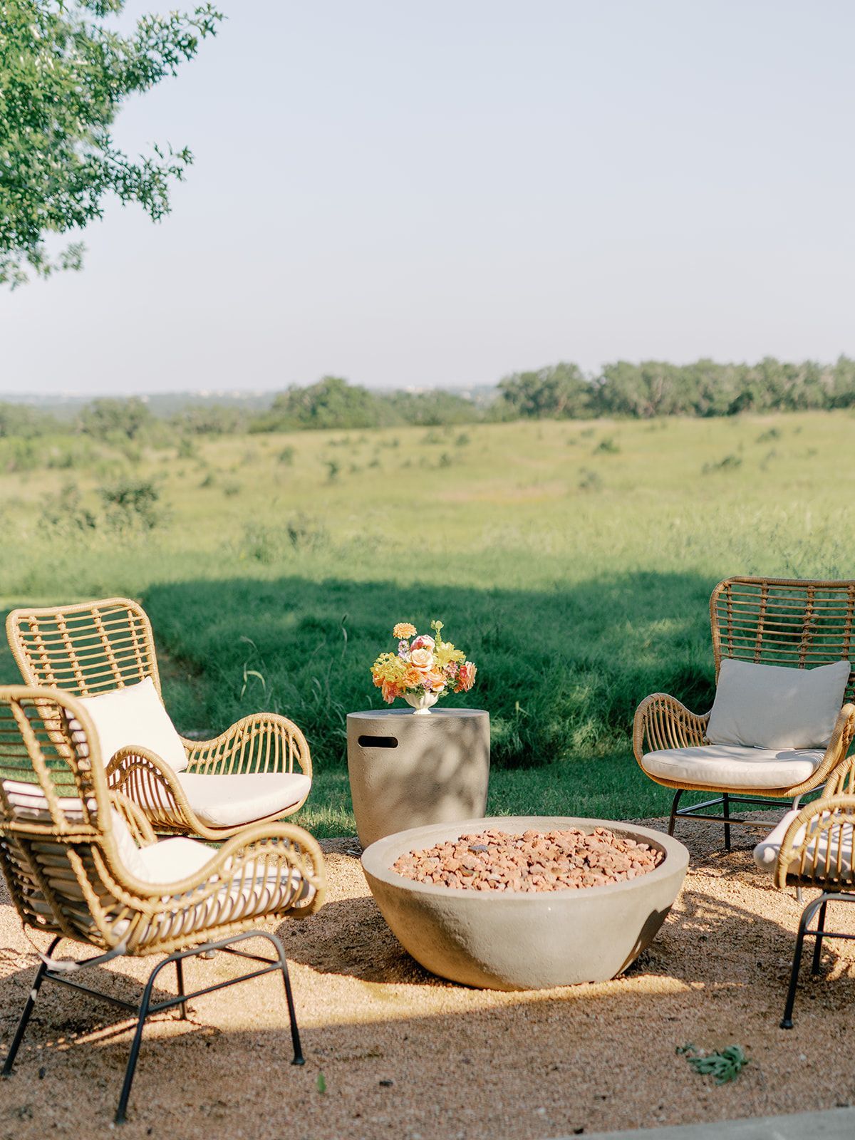 There is a fire pit in the middle of the patio with four wicker chairs around it. 