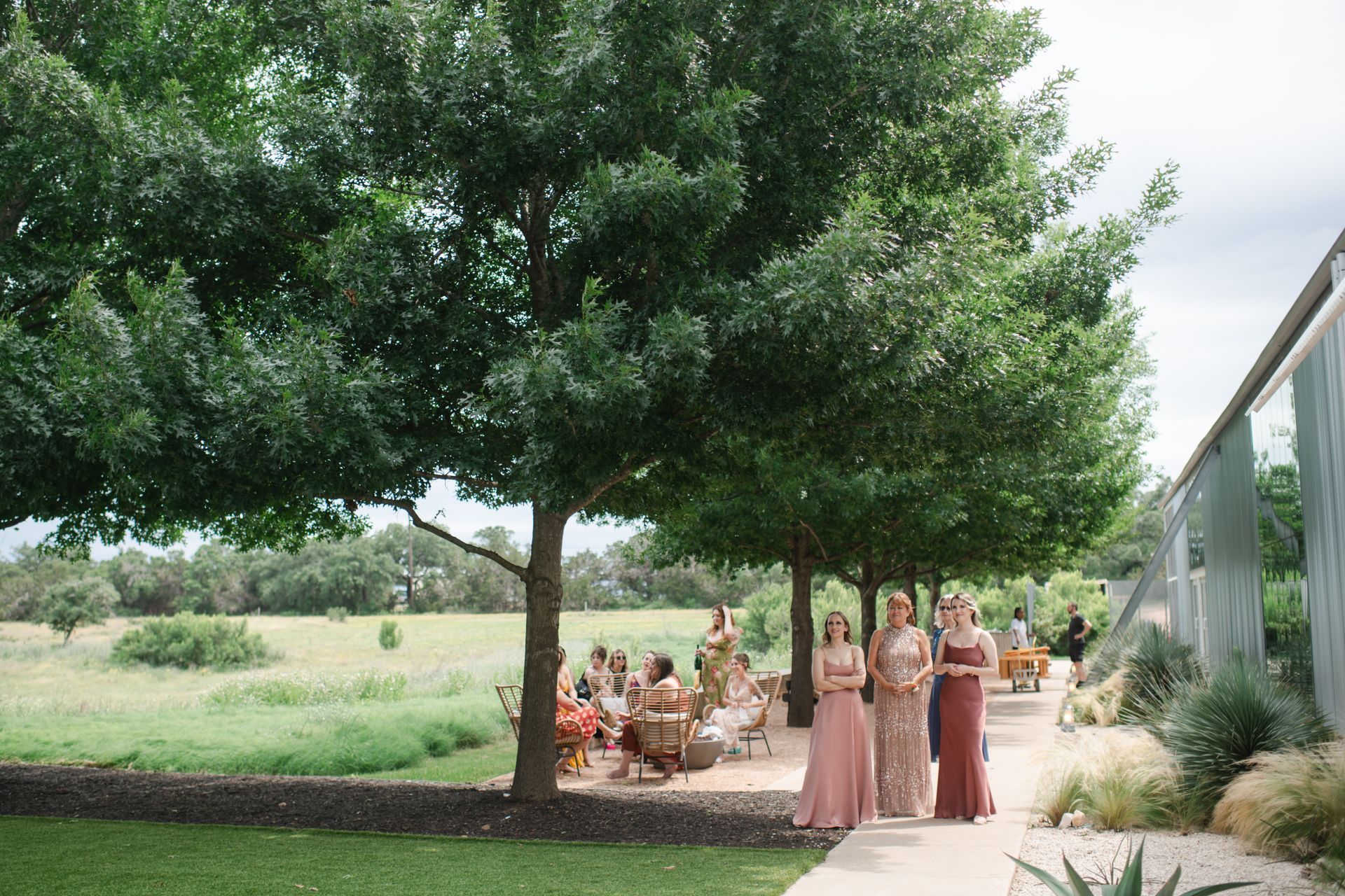 Bridesmaids in pink and burgundy dresses walking on a path next to a building and trees.