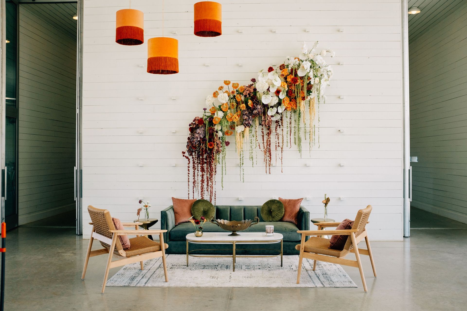 A modern lounge with a teal sofa, two chairs, floral arrangement, and hanging orange lights.