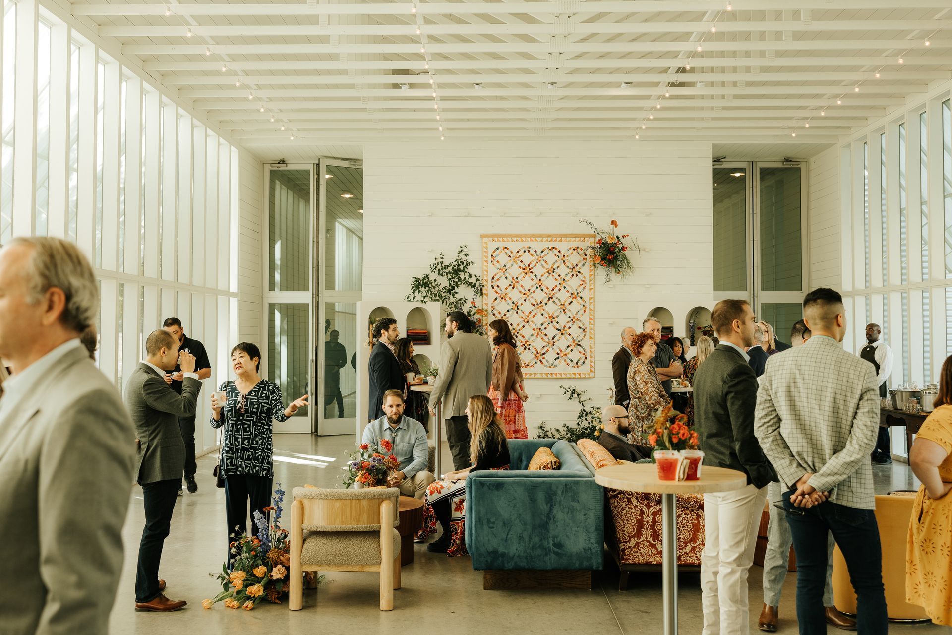 Guests mingling in a bright room with large windows, colorful furniture, and floral arrangements.