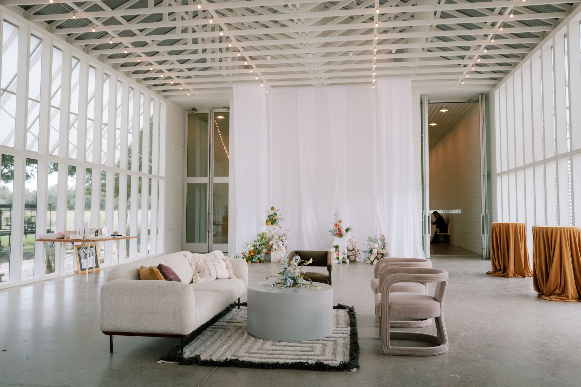 Modern venue with white walls, sofas, flowers, and tables set for an event.