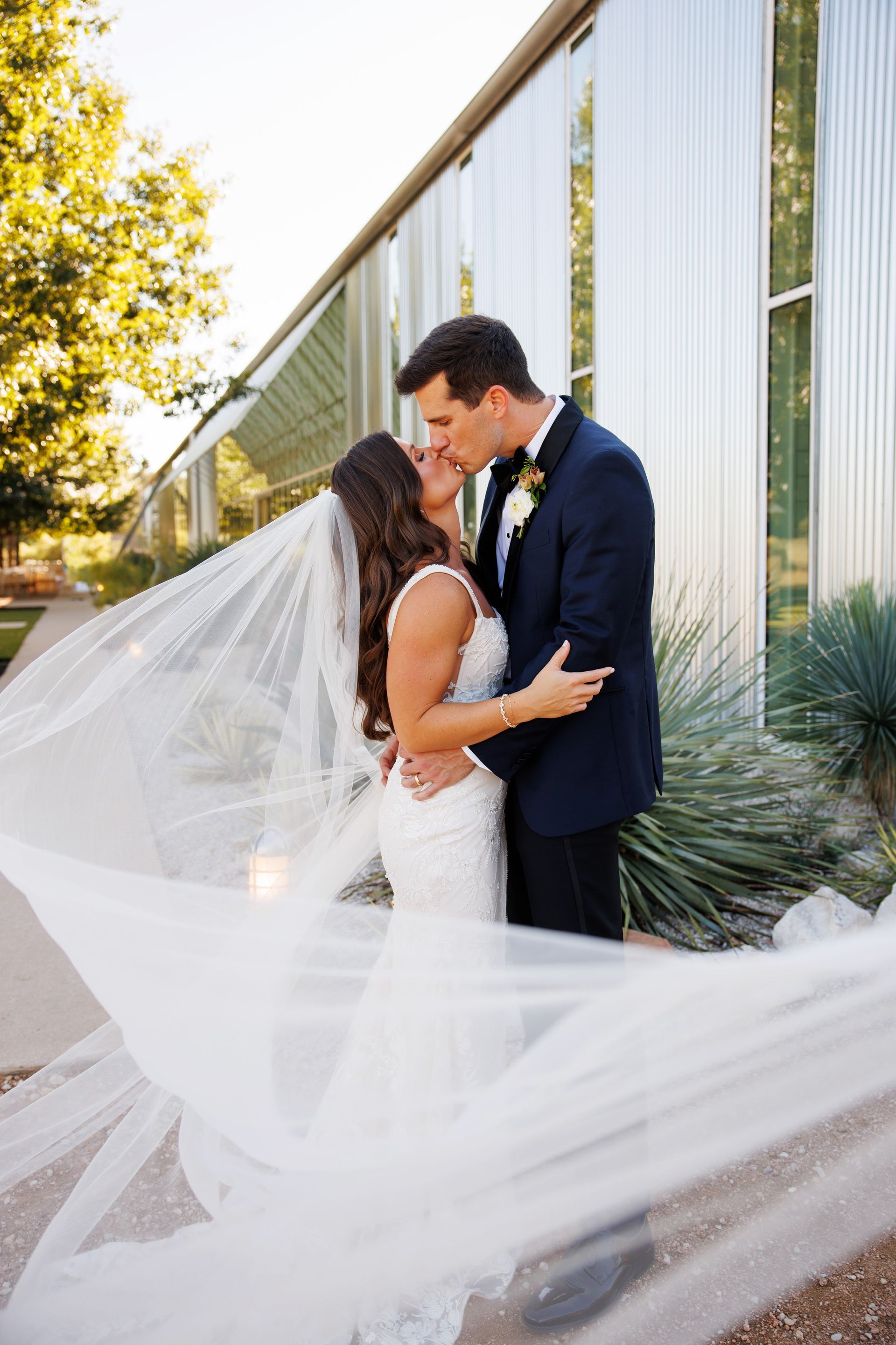 A bride and groom kissing with her veil blowing in the wind in front of the metal building. 