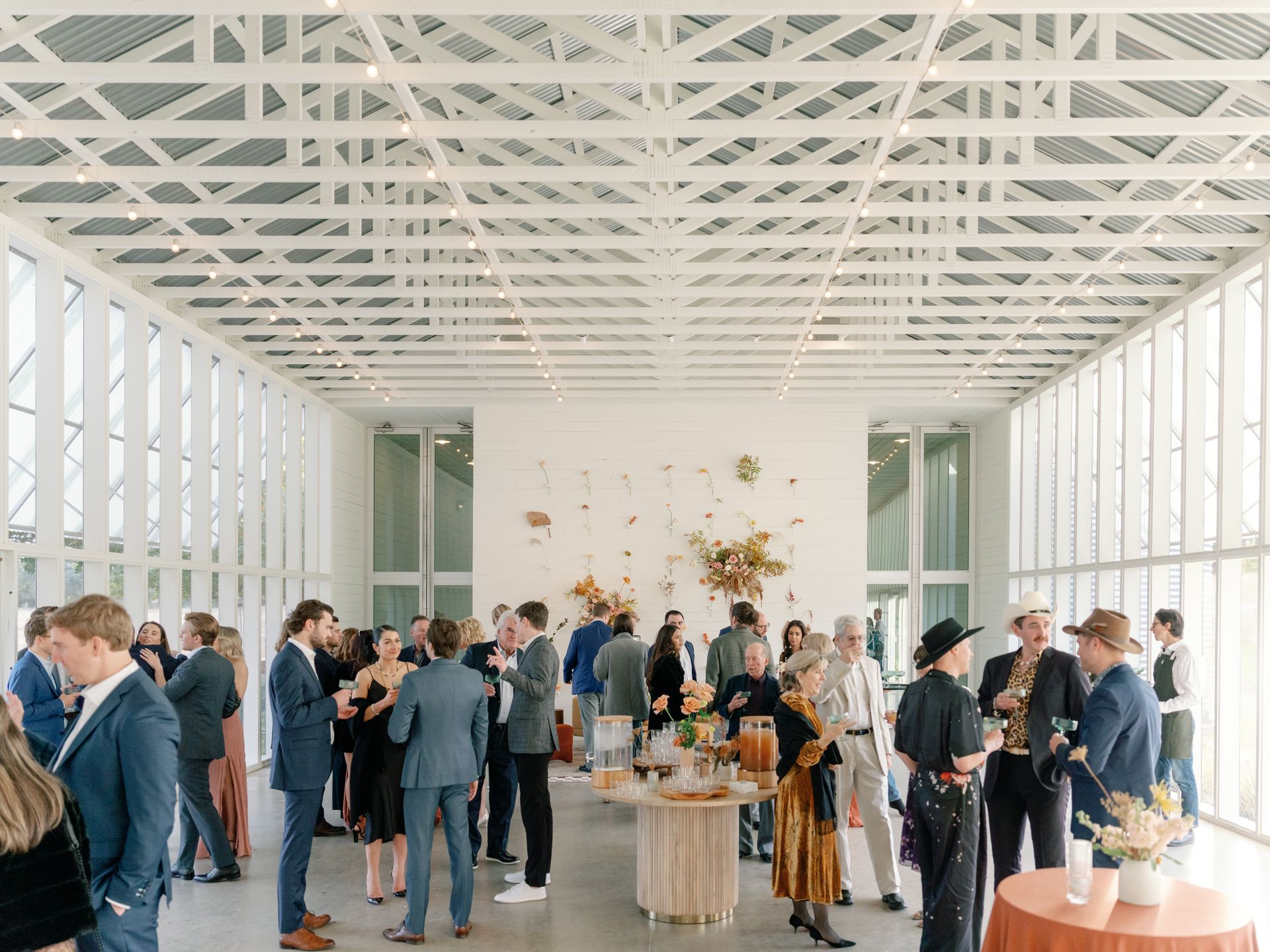 People socializing in a bright, modern room with large windows and floral decorations.