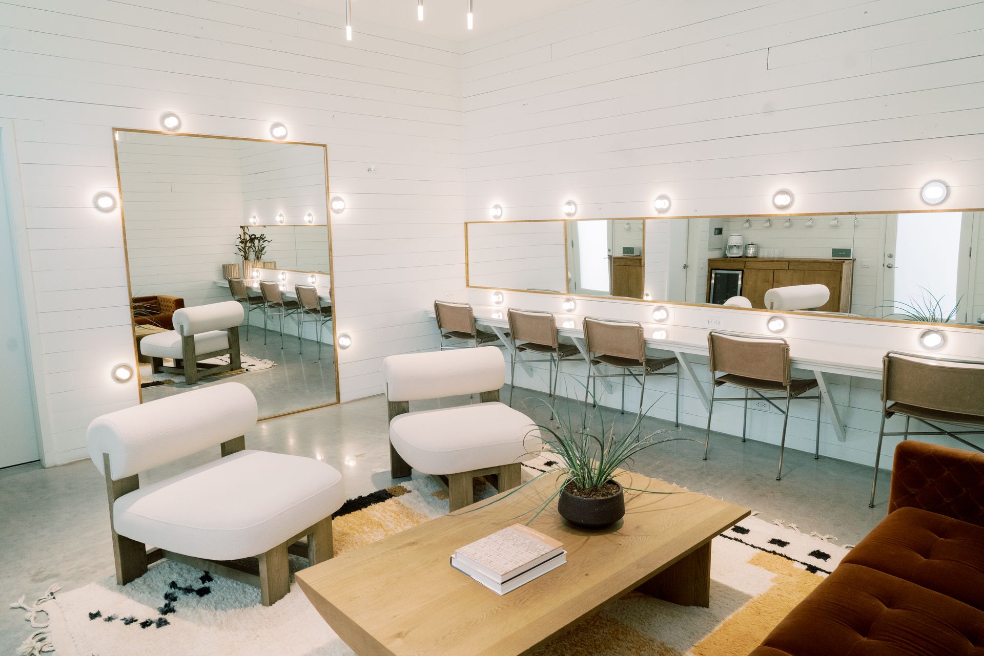 A dressing room with a tall mirror, couch, chairs, coffee table and long vanity mirror.