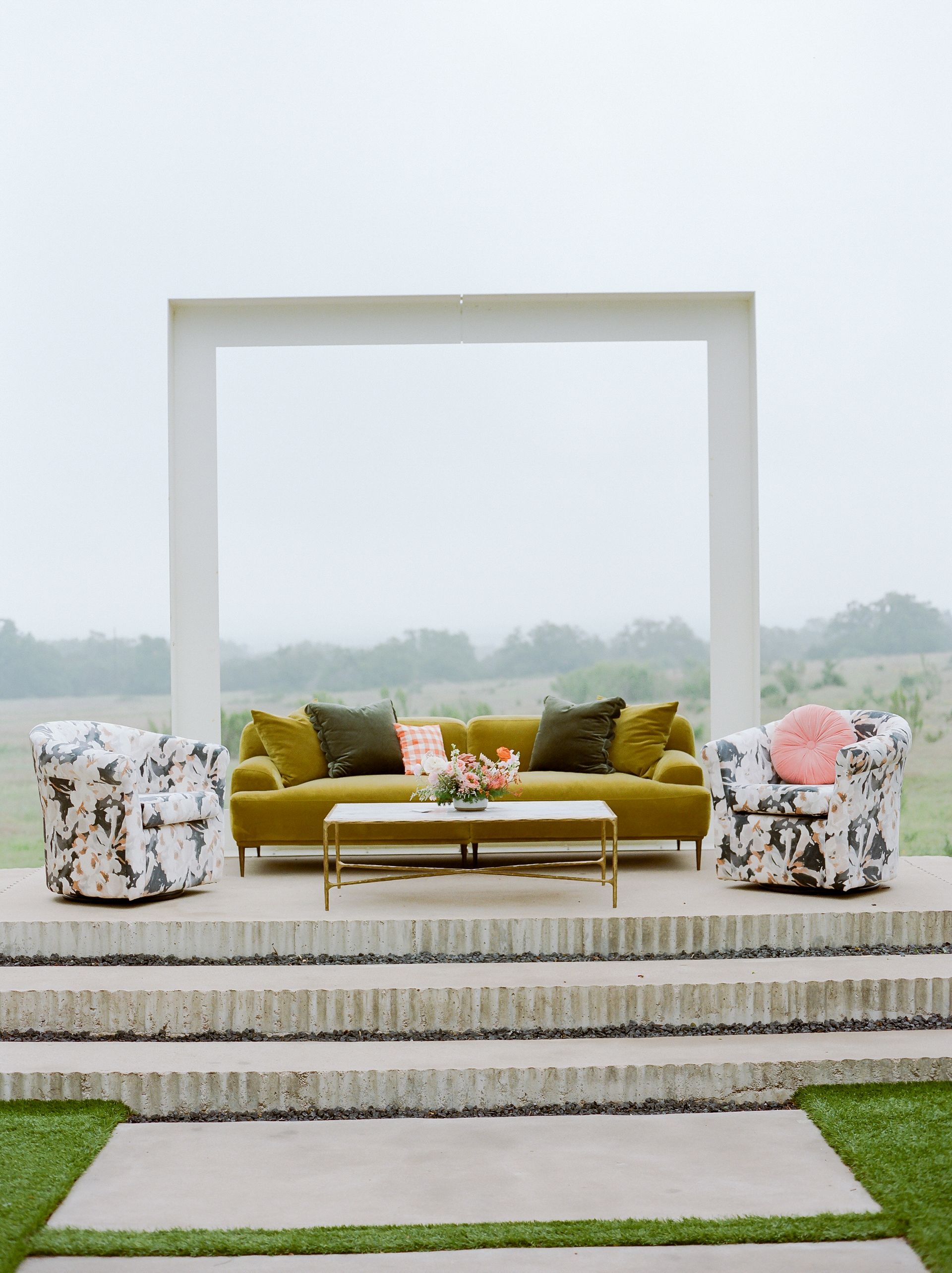 Olive green sofa and patterned armchairs on a raised platform in an outdoor setting.