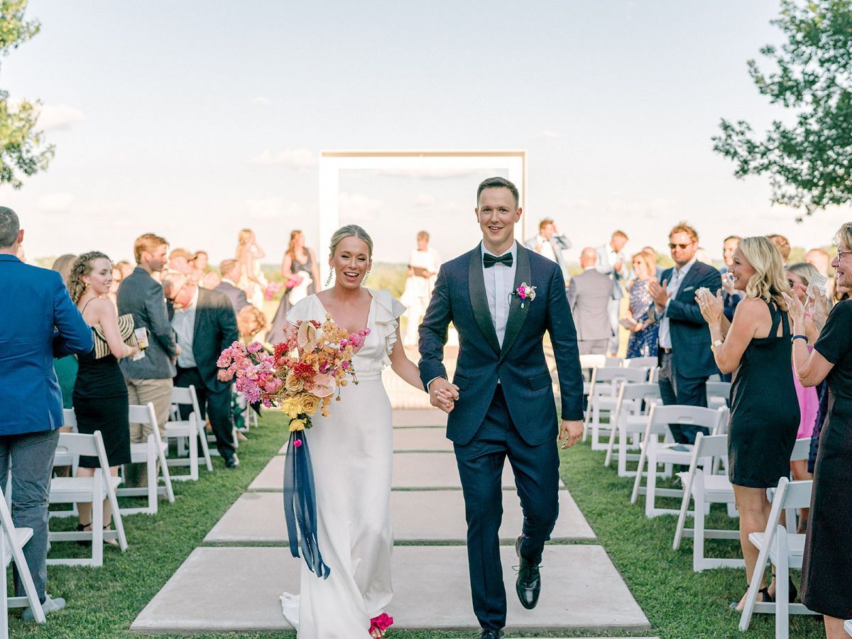 A bride and groom are walking down the aisle at their wedding holding hands.