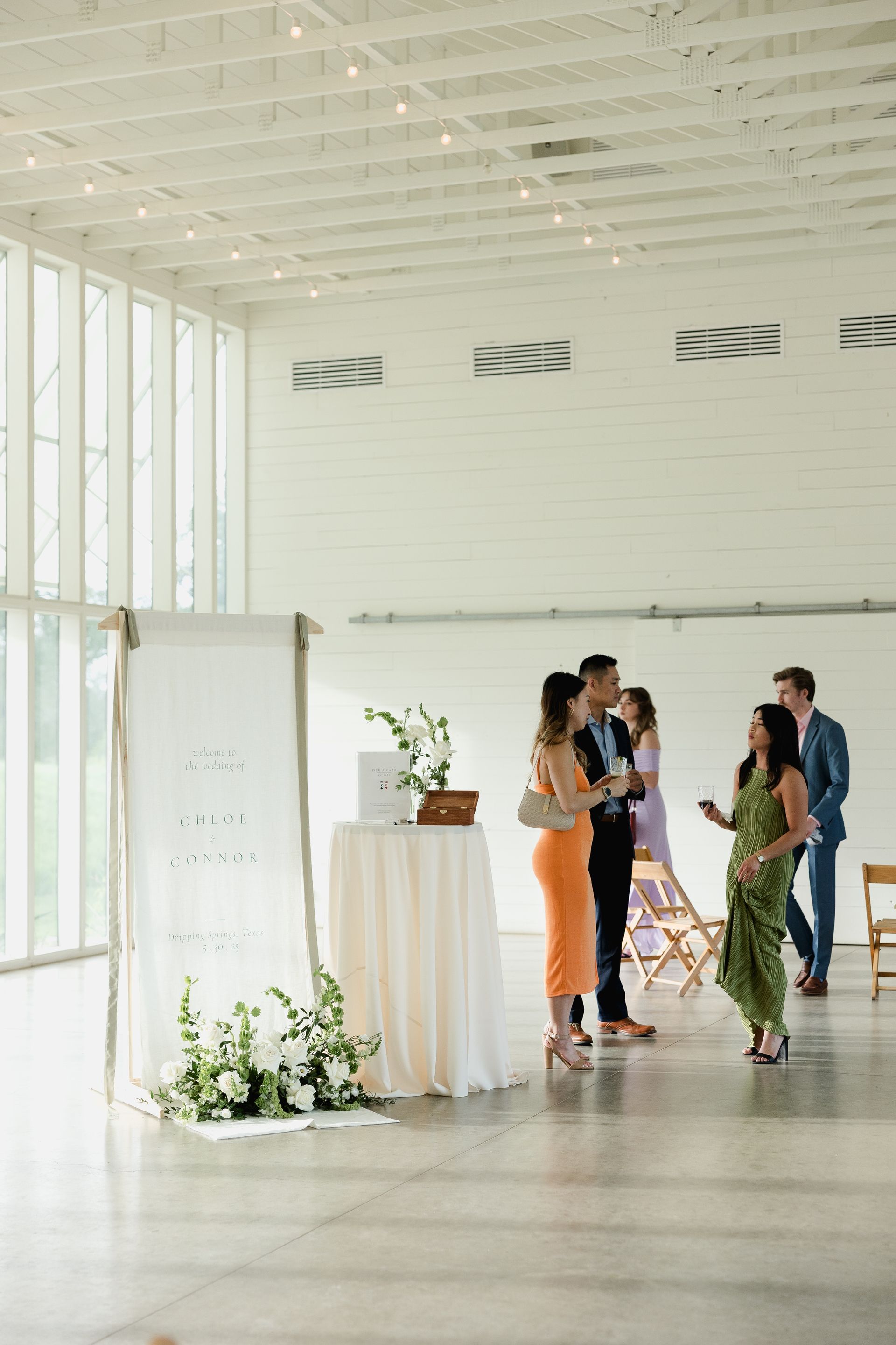 Wedding reception at Prospect House with guests socializing near a sign and a draped table in a white-walled room.