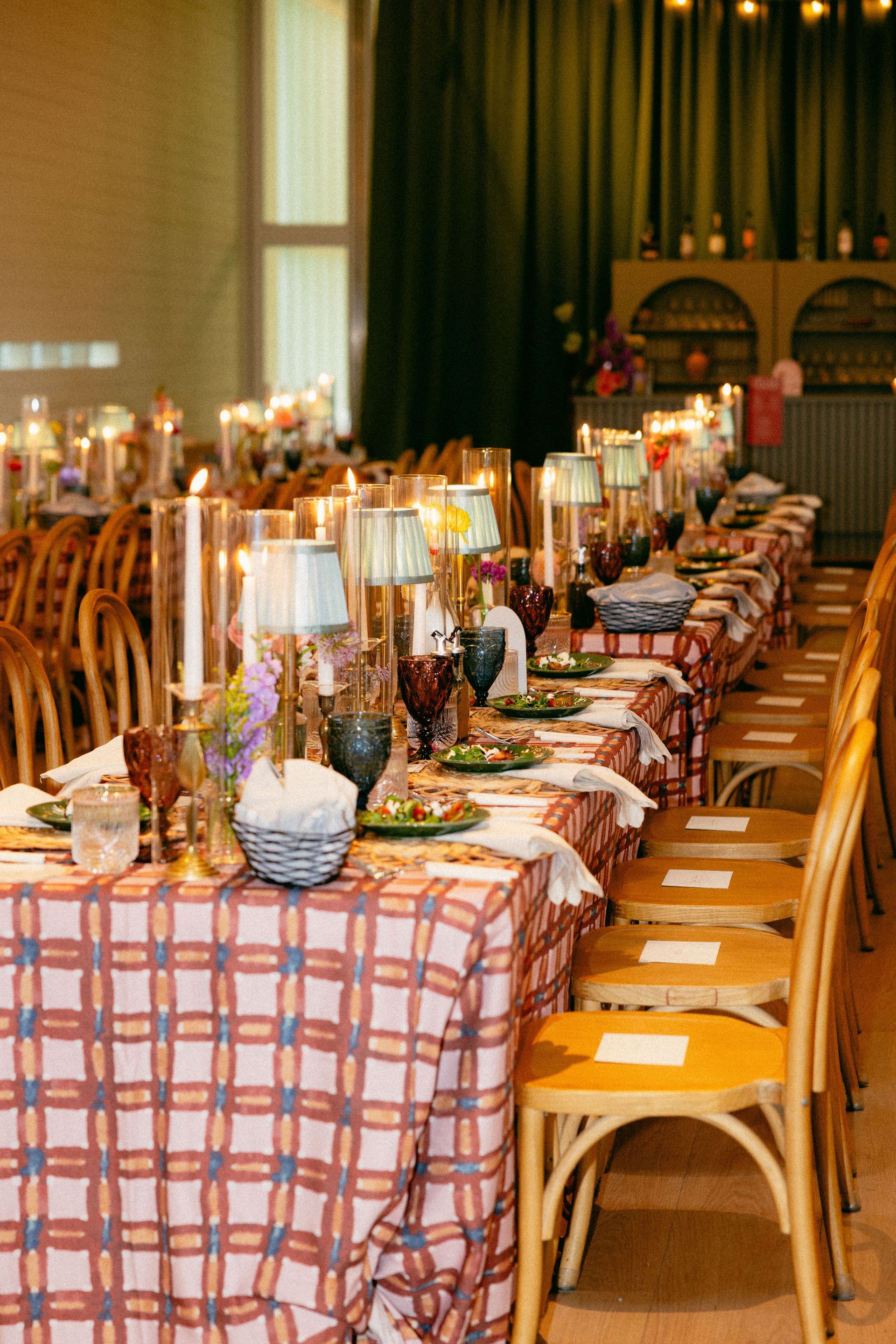Long banquet table set for a dinner party with a plaid tablecloth and ornate place settings, indoors.