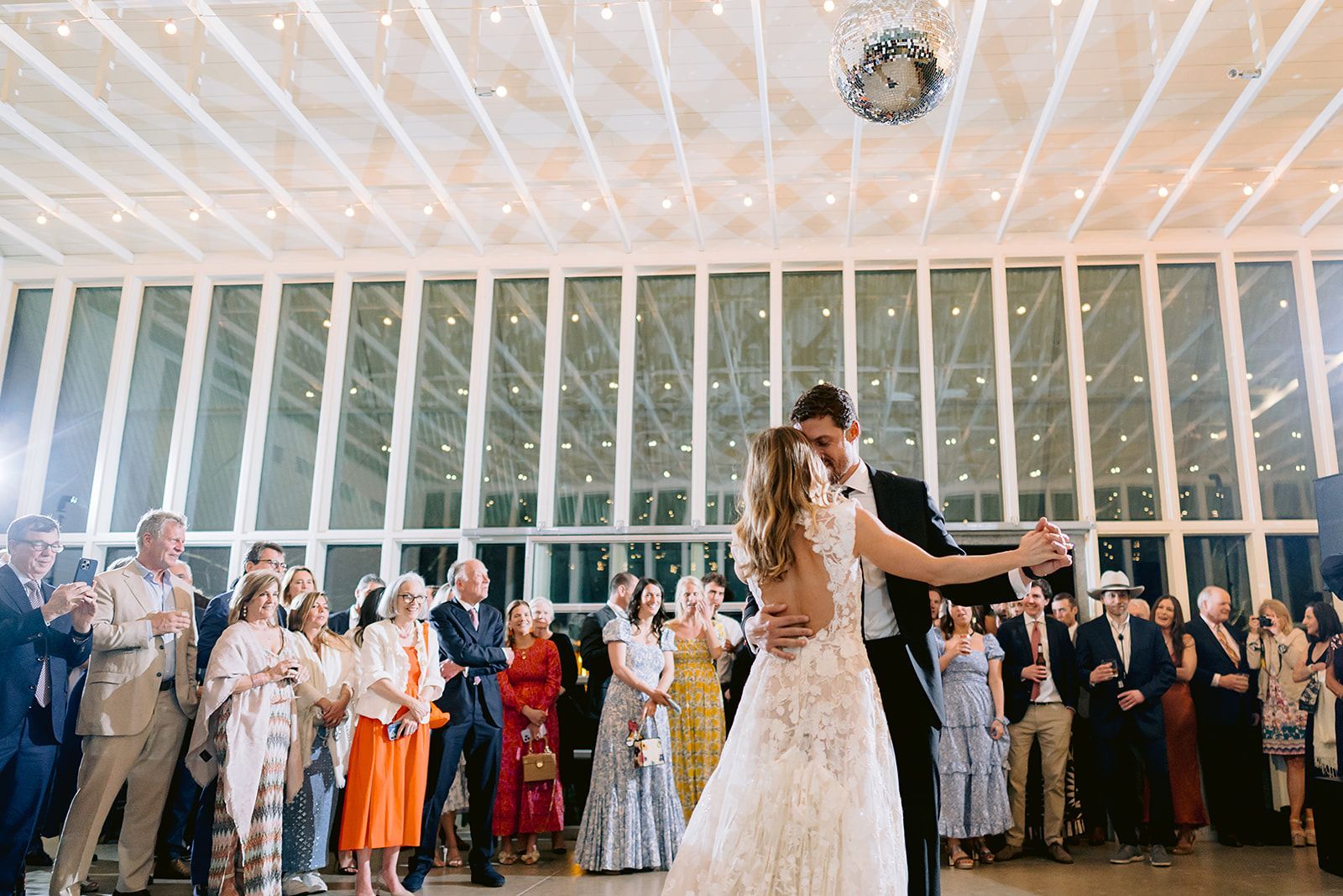 A bride and groom are dancing their first dance at their wedding reception with family and friends surrounded.