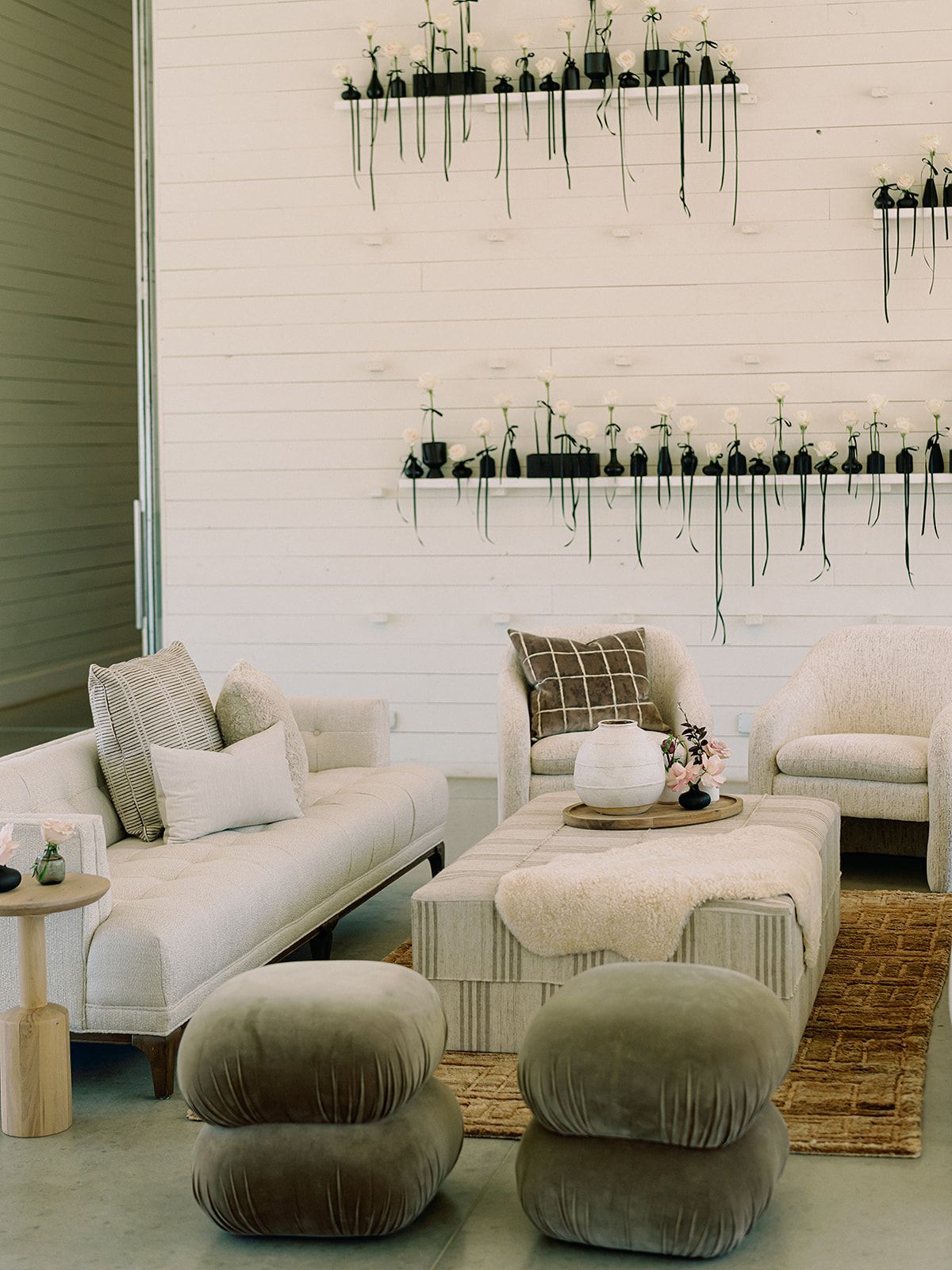 Cozy set up at Prospect House Gallery room with white walls, sofa, armchairs, ottoman, and art. Two velvet poufs in front.