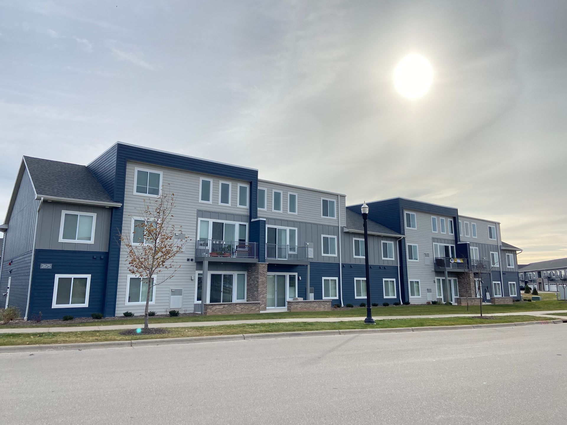 Modern apartment building with blue and gray siding under a bright sun on a quiet street
