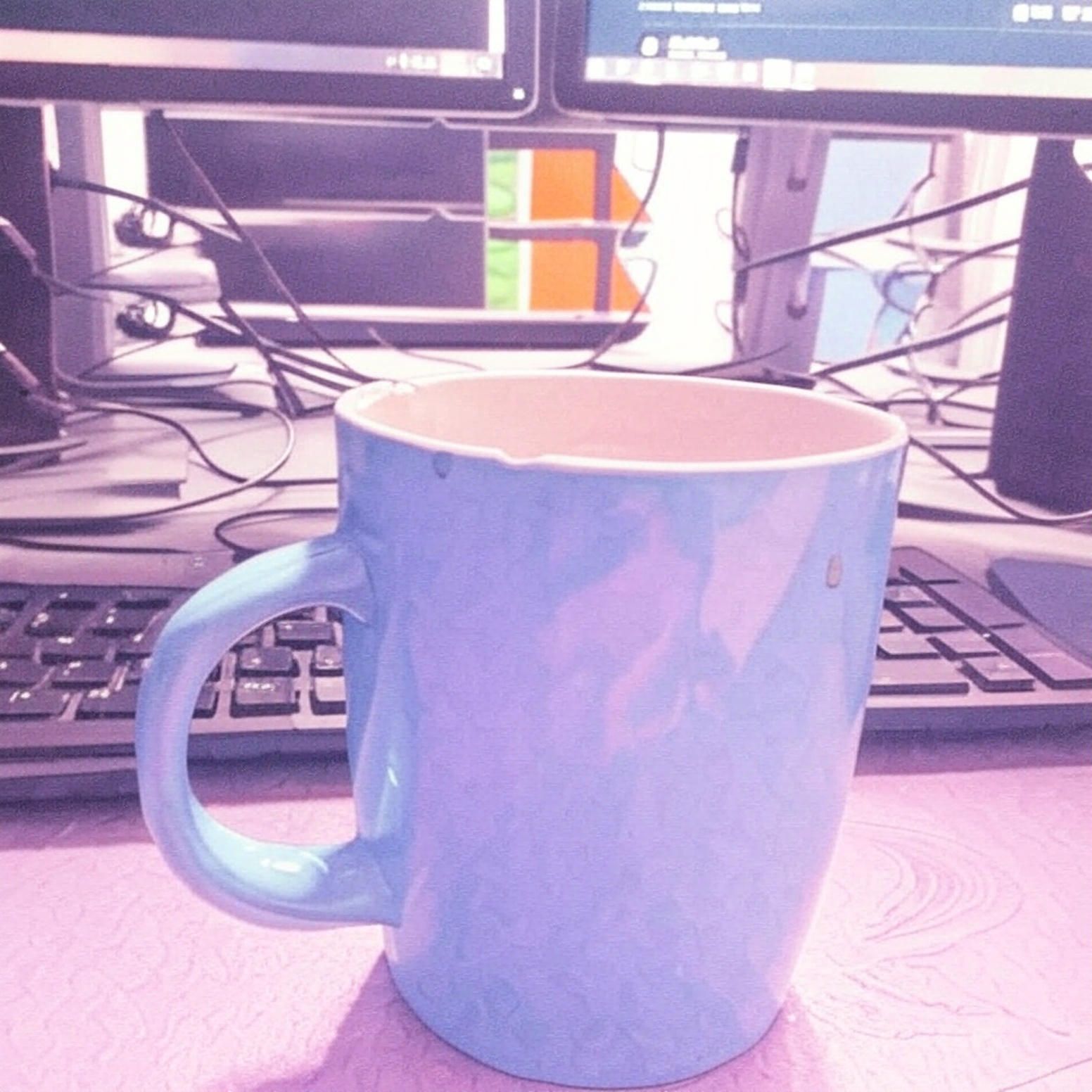 Een blauwe koffiemok staat op een bureau voor een computermonitor