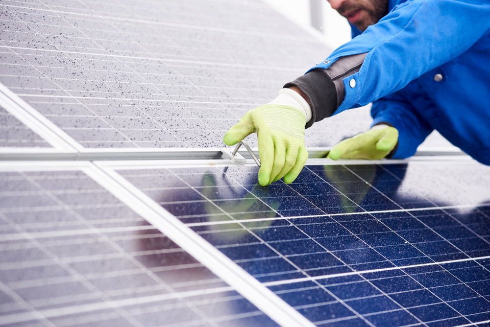 A Man Wearing Green Gloves Is Working on A Solar Panel — Brent Hawe Solar & Electrical in Glenfield Park, NSW
