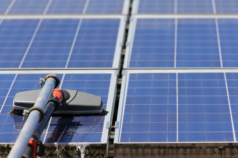 A Man Is Kneeling on Top of A Solar Panel While Using a Laptop — Brent Hawe Solar & Electrical in Glenfield Park, NSW