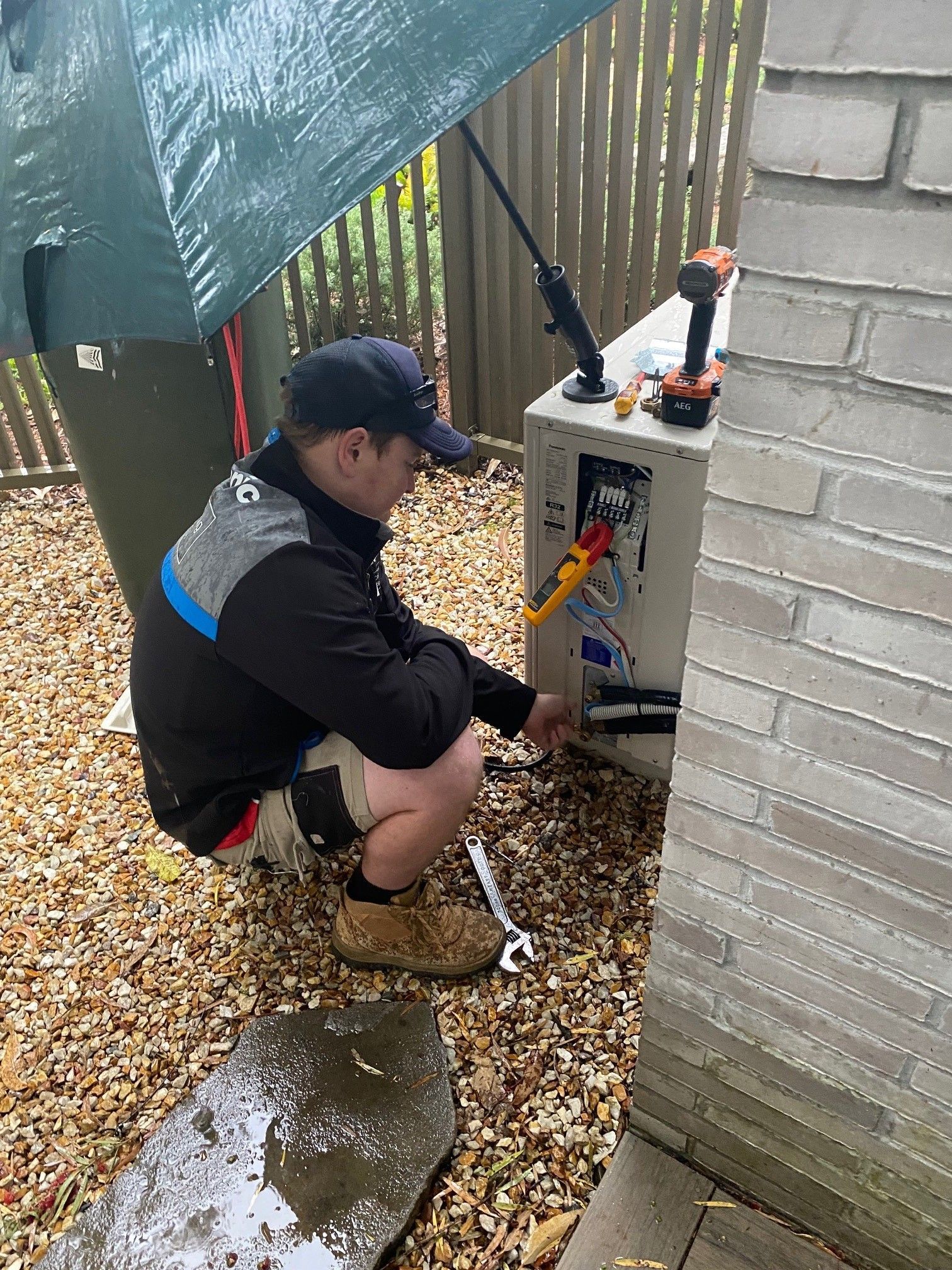 Electrician working on outdoor electrical panel, under an umbrella— Coolman Airconditioning in Goonellabah, NSW