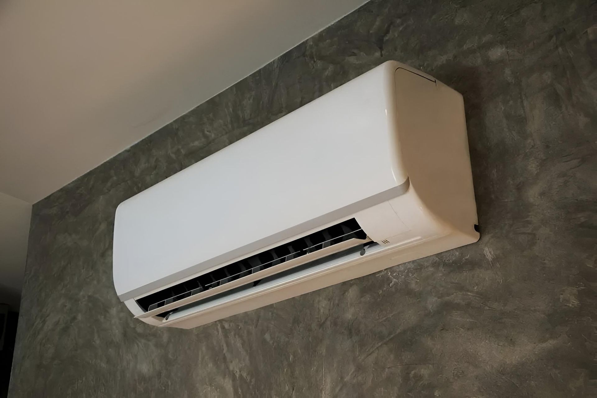White air conditioning unit mounted on a textured gray wall — Coolman Airconditioning in Broken Head, NSW