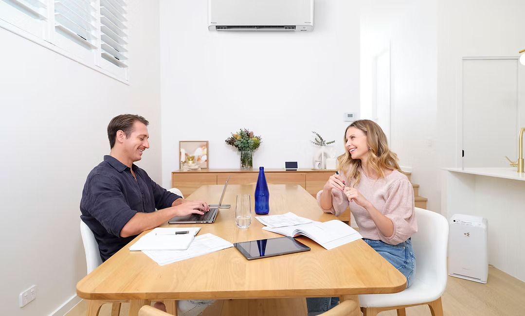 Man and woman at a table, using a laptop and paperwork in a well-lit room, smiling and talking— Coolman Airconditioning in Broken Head, NSW