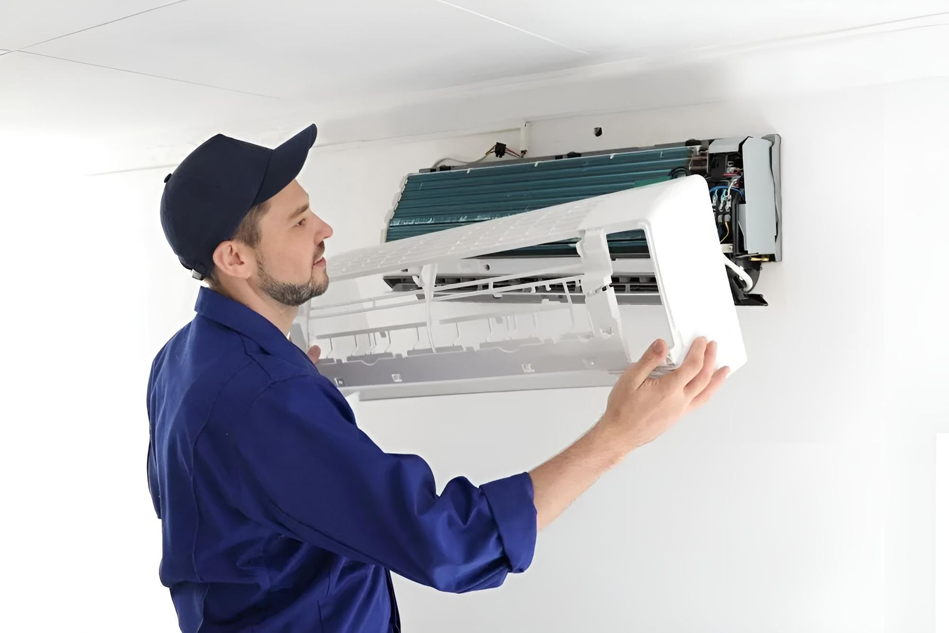 Technician in uniform servicing a wall-mounted air conditioner by removing the front cover panel.