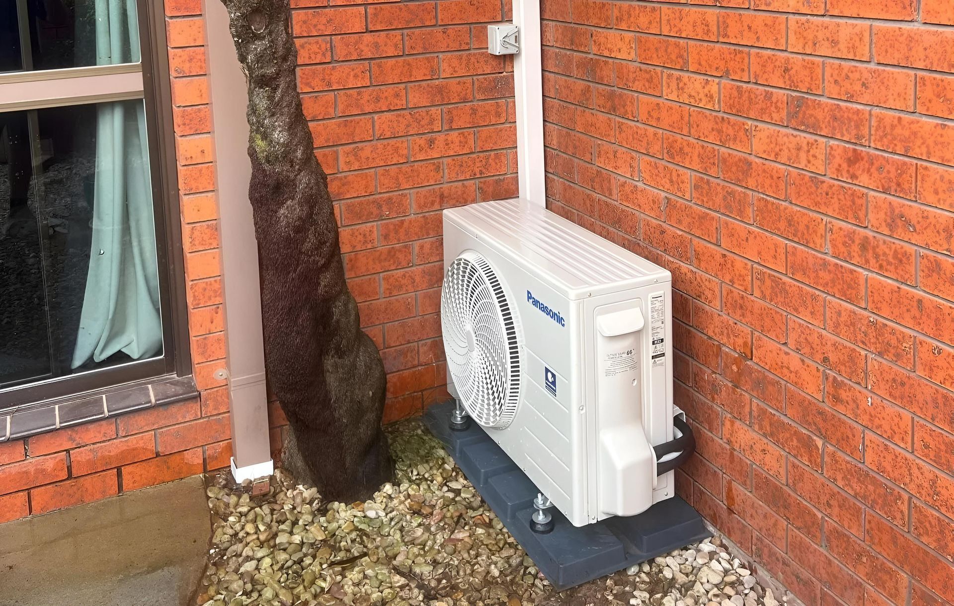 An Air Conditioner unit is outside a brick wall house — Coolman Airconditioning in Broken Head, NSW