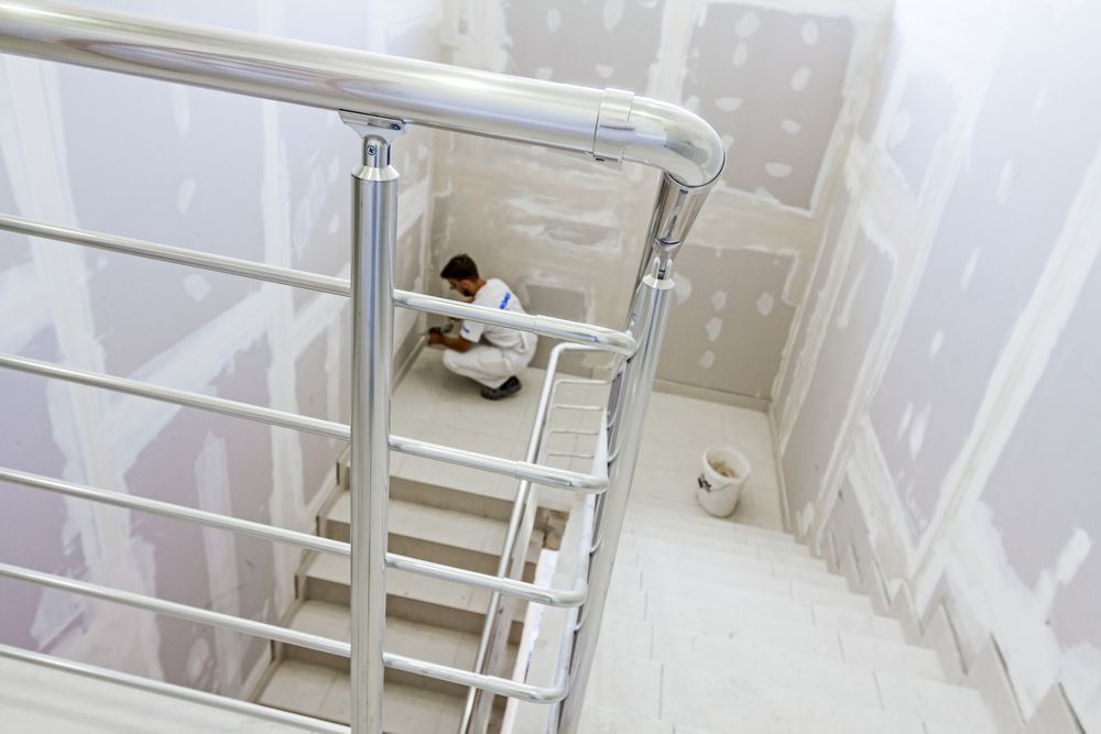 Man Working on Drywall in A Stairwell with Metal Handrails — Completely Plastered North Coast in Goonellabah, NSW
