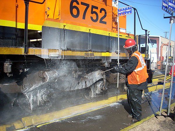Hulcher crew member pressure washes the wheel set of a locomotive