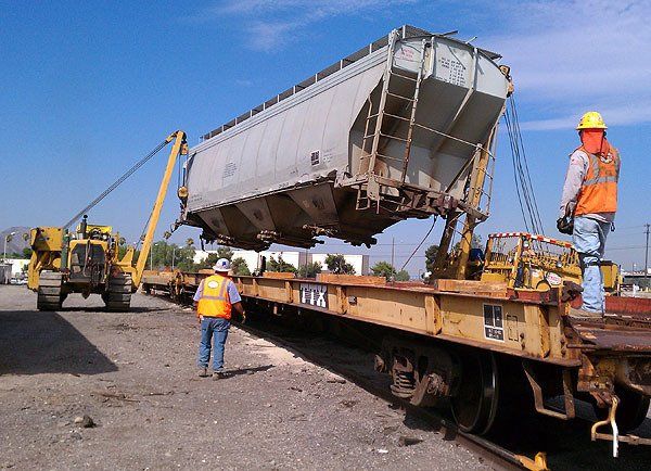 Hulcher sidebooms load a damaged hopper car onto a rail car for transport to the scrap yard during a load-out / tie down project