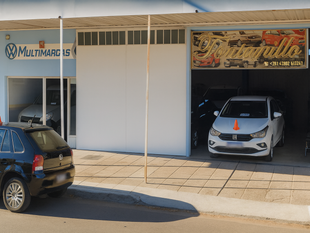 Escaparate de concesionario de automóviles con coches en exposición; edificio de color azul claro y blanco, soleado.
