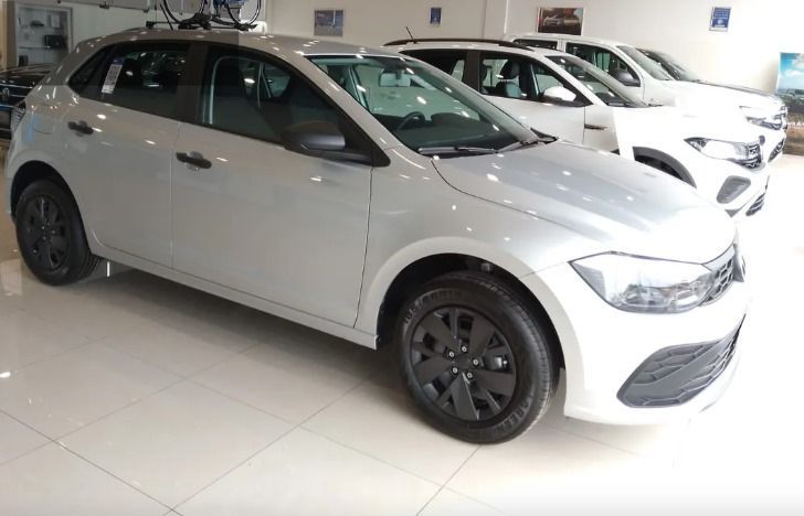 Un hatchback plateado con llantas negras en una sala de exposición. Se ven otros vehículos al fondo.