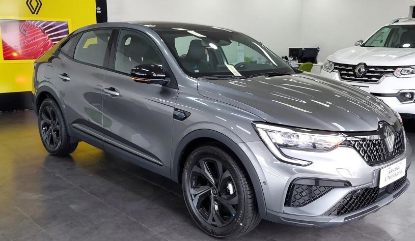 SUV Renault Arkana coupé color gris en sala de exposición, llantas negras, techo oscuro, otro vehículo detrás.