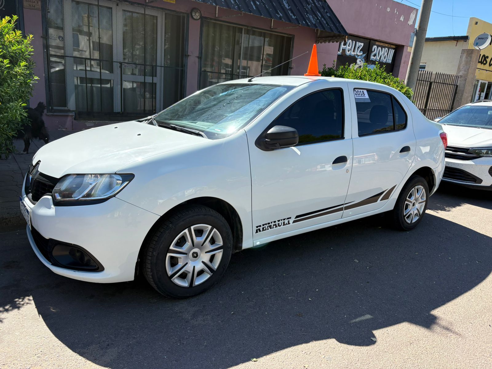 Sedán Renault blanco estacionado en una calle de la ciudad; cono naranja en el techo.