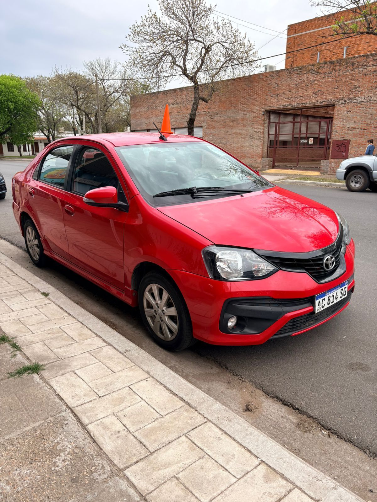 Automóvil Toyota rojo estacionado al costado de una calle con un edificio de ladrillo al fondo.