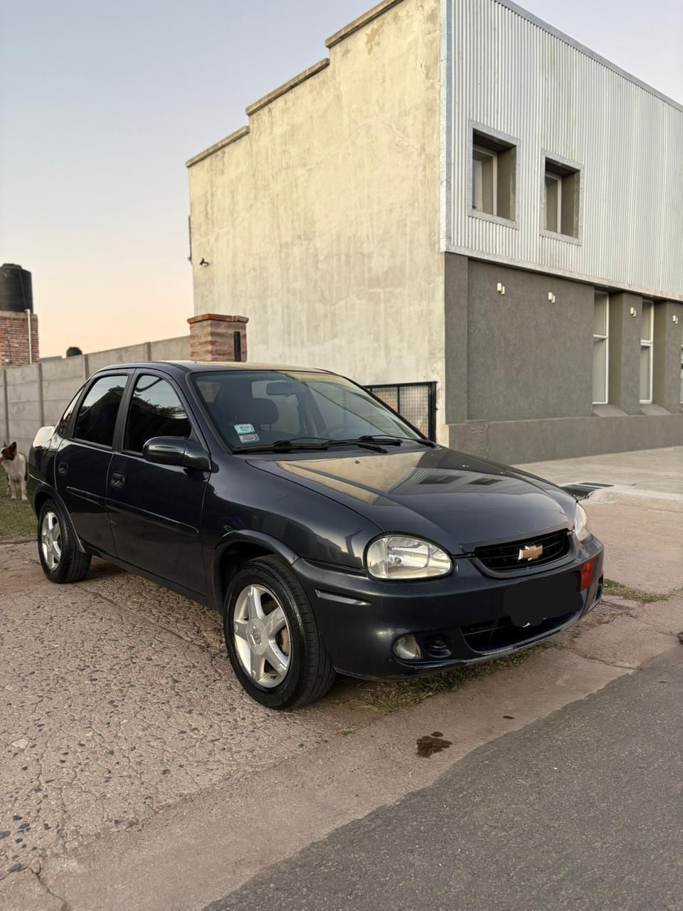 Un Chevrolet Corsa azul oscuro estacionado en una entrada pavimentada frente a un edificio.
