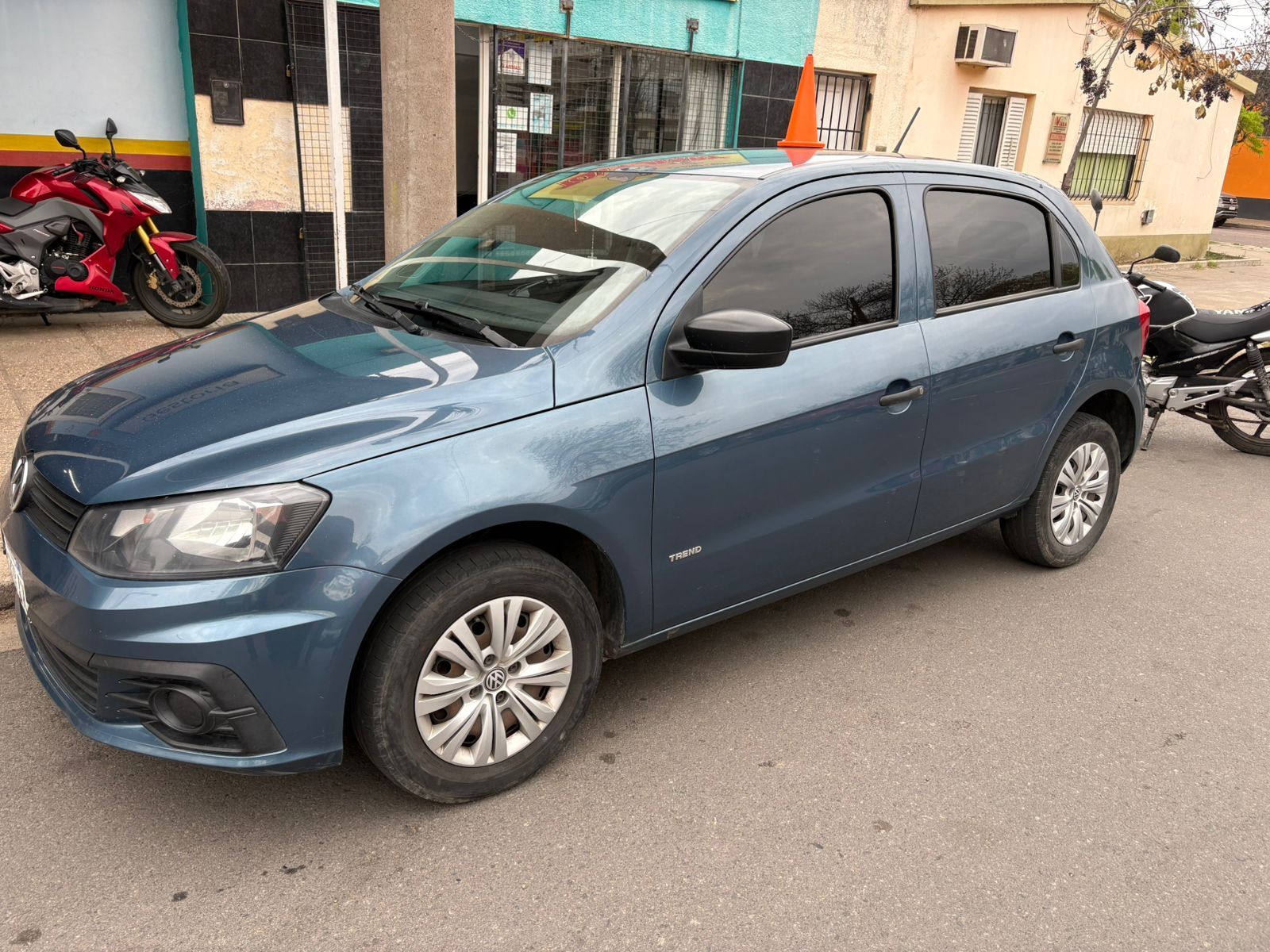 Volkswagen hatchback azul estacionado en una calle frente a una tienda.