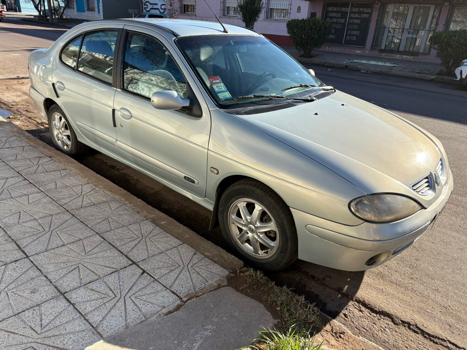 Renault Mégane plateado aparcado en la acera de una calle de la ciudad.