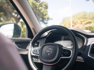 Interior de un automóvil Volvo, con el volante enfocado, el espejo lateral y árboles visibles afuera.