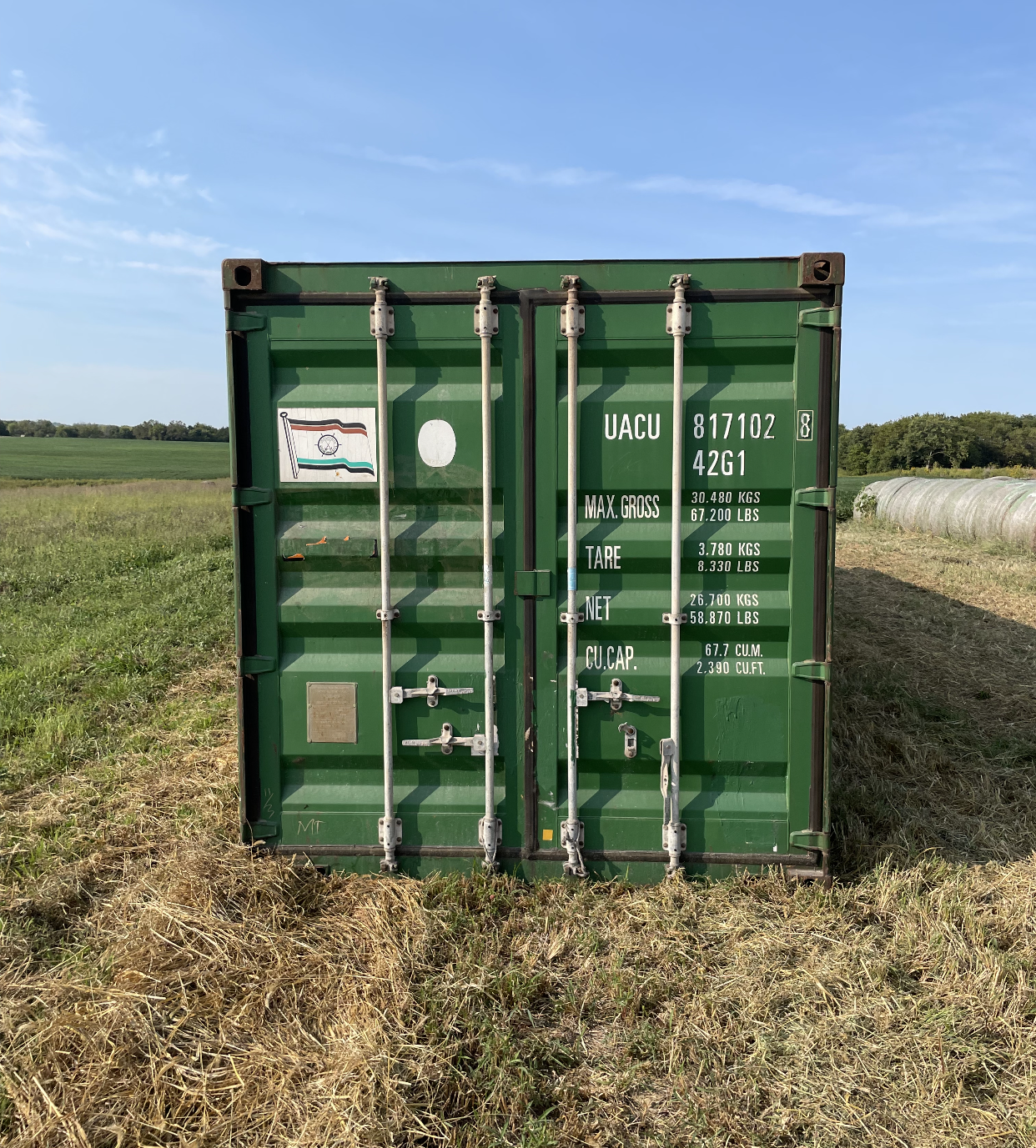 A green shipping container is sitting in the middle of a field