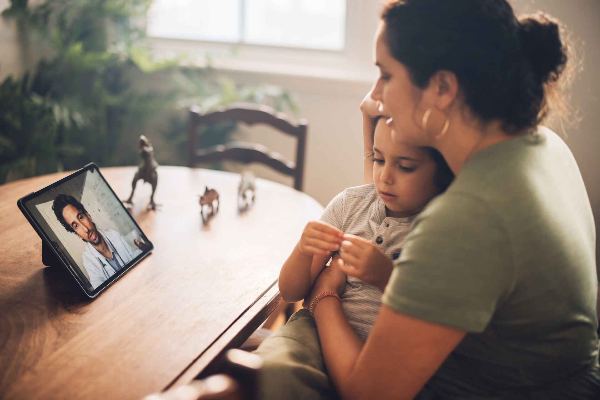 Mother holding her sick female toddler while on a video call with a healthcare professional at home.