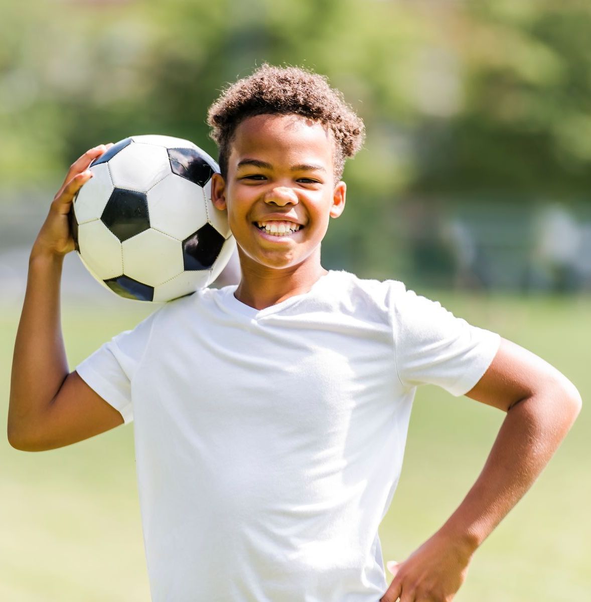 image of a young black male teen holding a soccer ball up on his shoulder smiling.