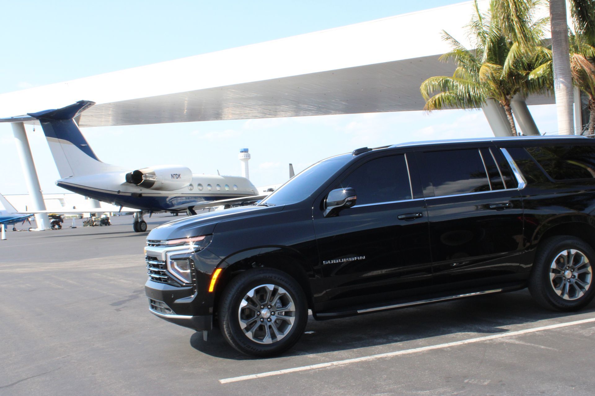 Black SUV parked at an airport with private jets in the background on a sunny day.
