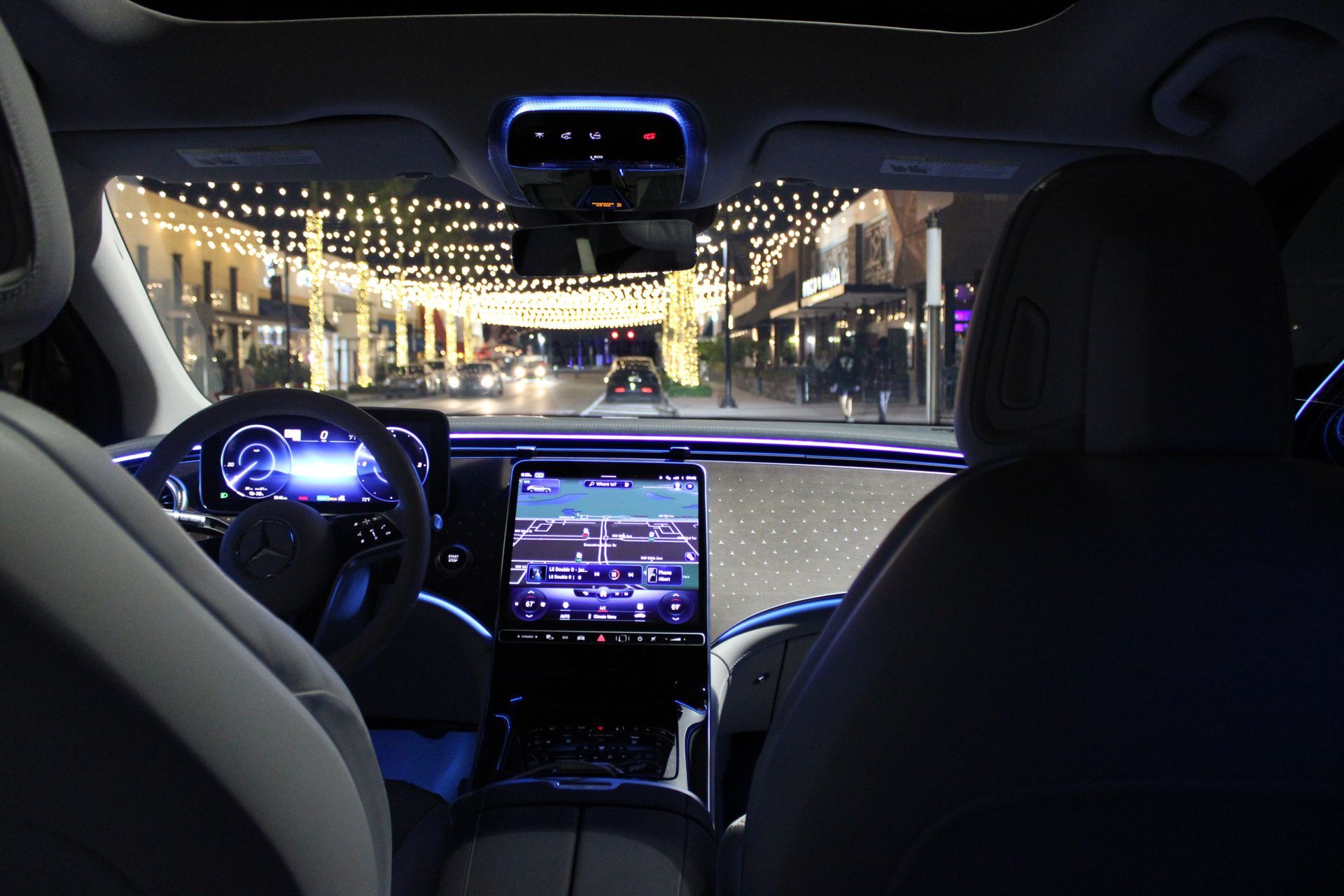 Interior car view at night, looking out at a street with lights. Blue dashboard displays.