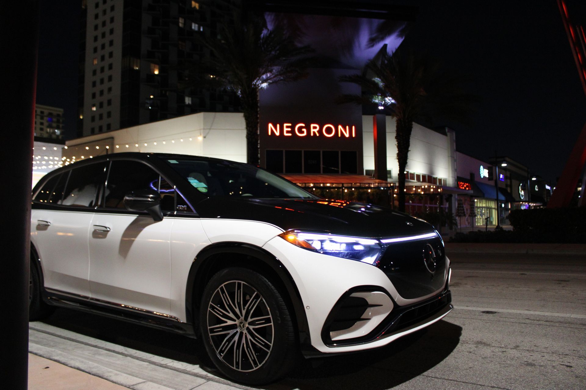 White and black Mercedes SUV parked on a city street at night in front of a Negroni restaurant.