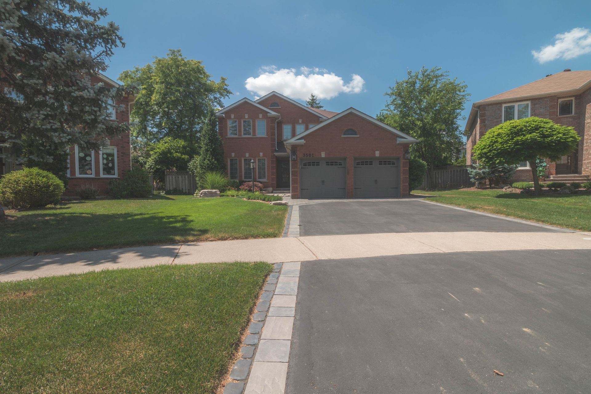 A brick house with two garage doors is in a residential neighborhood.